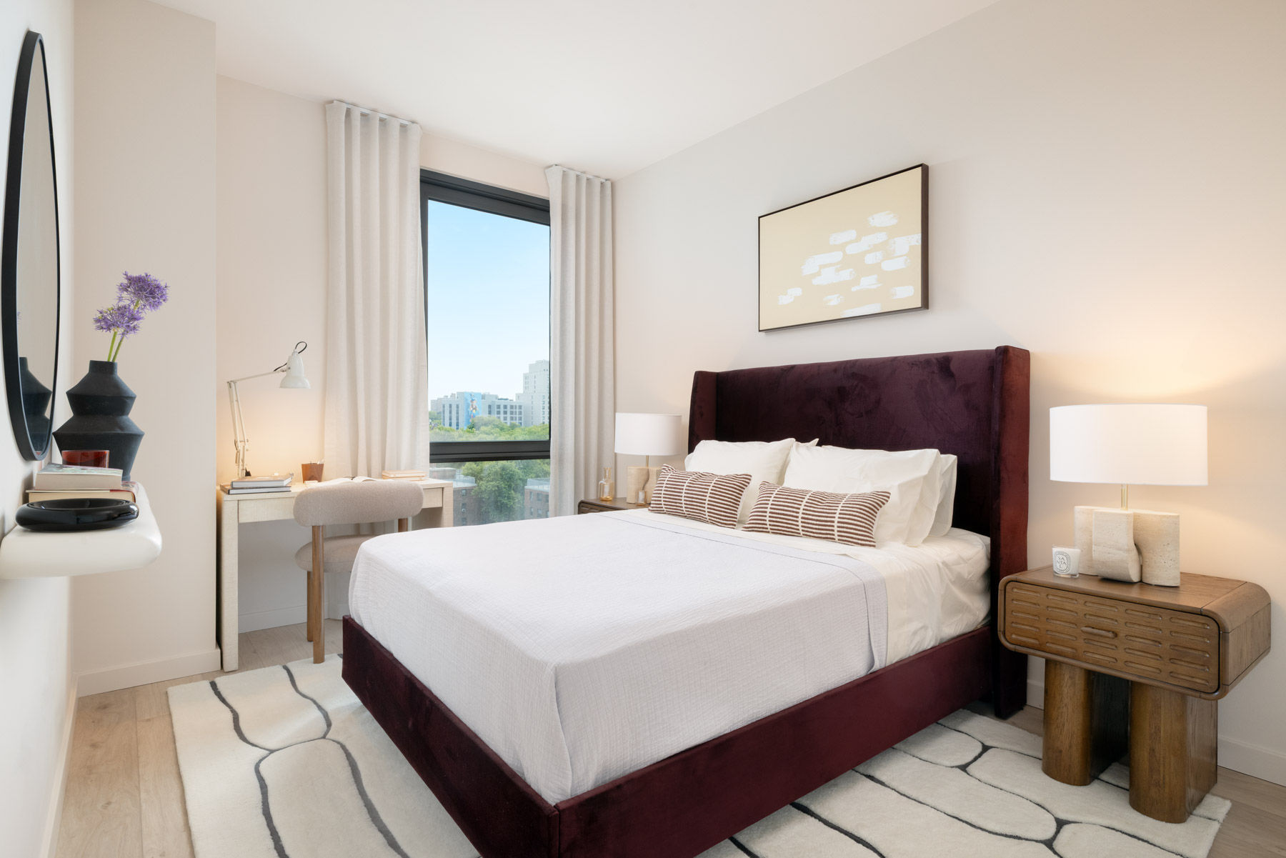 Bright modern bedroom with seating area and large window, nightstands with lamps