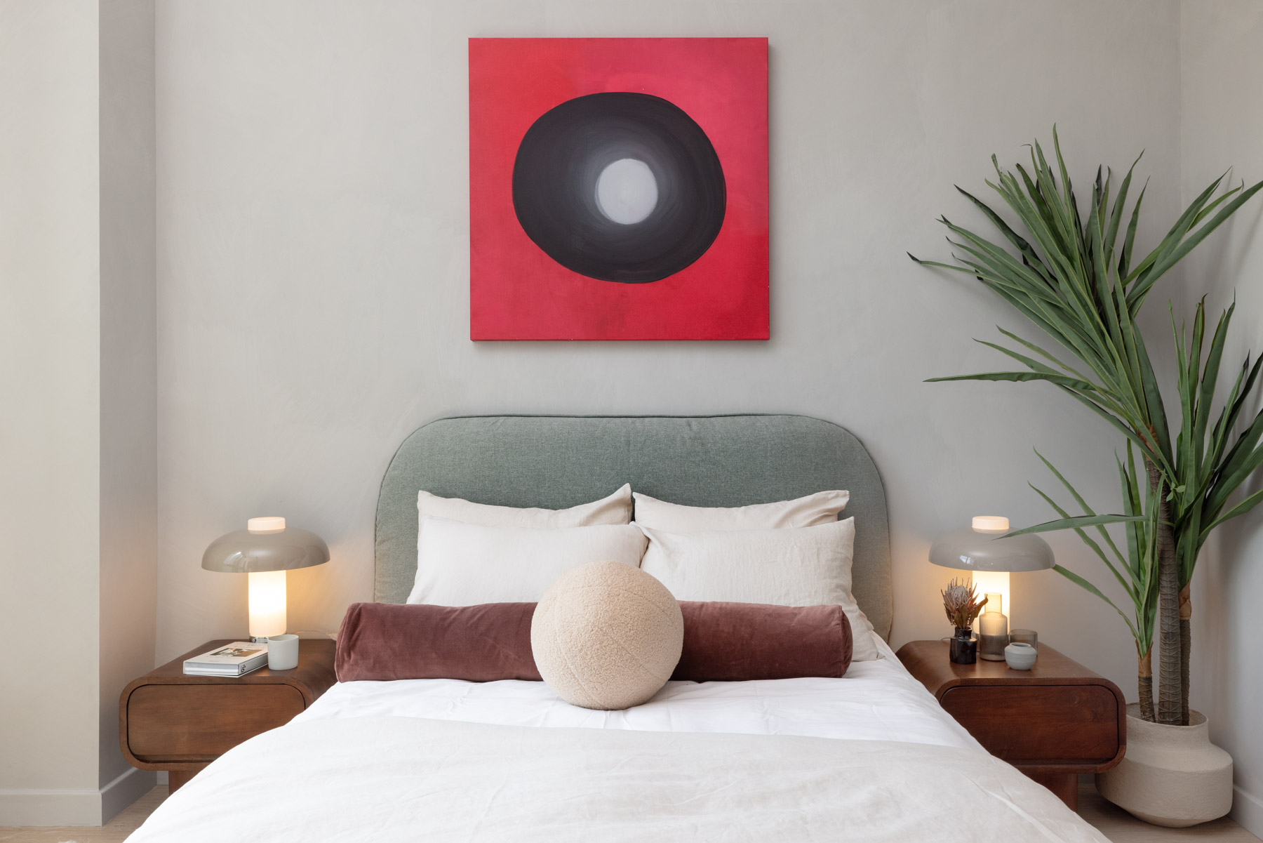 Bedroom detail with modern nightstands with lamps and large modern art on wall behind, floor plant in corner