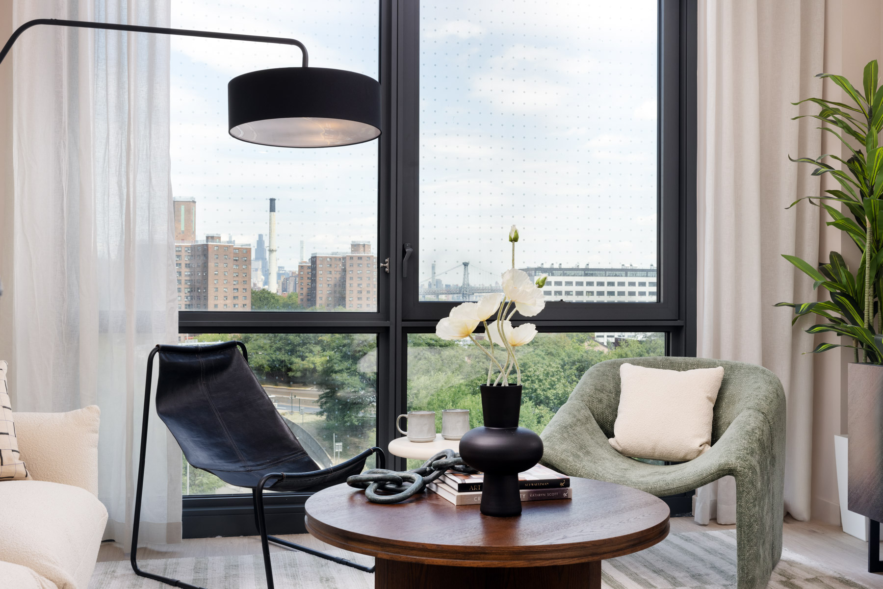 Living room detail showing round wood coffee table, vase with flowers and seating near large window and lamp