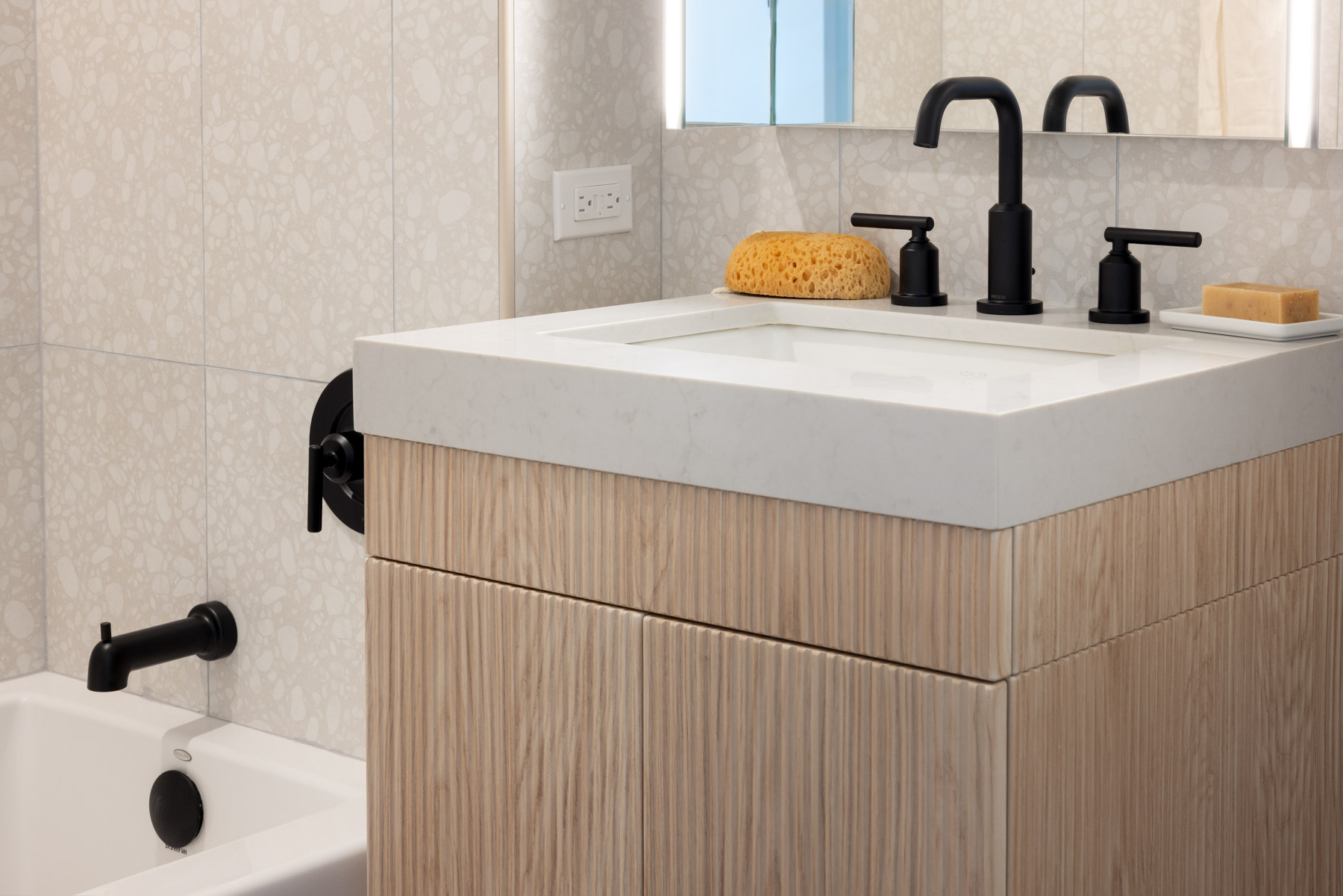 Bathroom sink detail showing Light Wood Laminate, London Grey Stone Countertops with dark fixtures