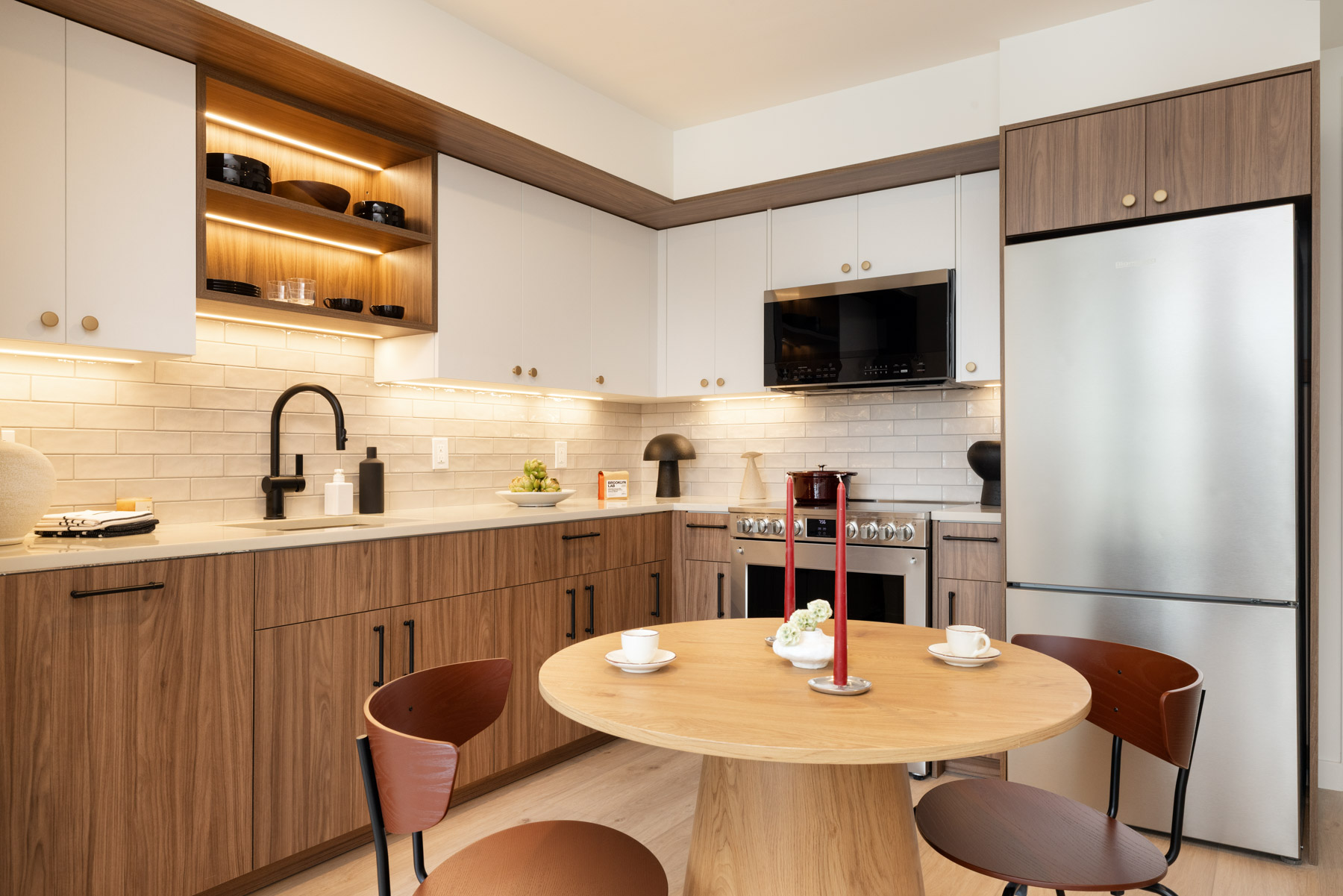 Kitchen detail showing round eating table, sink with dark fixtures, White Upper/Dark Walnut cabinets, London Grey Quartz Countertops and Stainless Steel Appliances