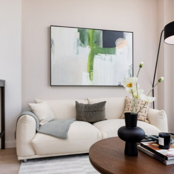 Living room detail of light colored couch with large modern painting above and wood coffee table with vase and flowers
