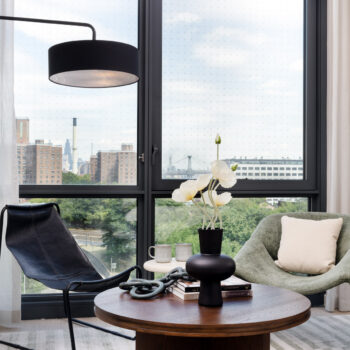 Living room detail showing round wood coffee table, vase with flowers and seating near large window