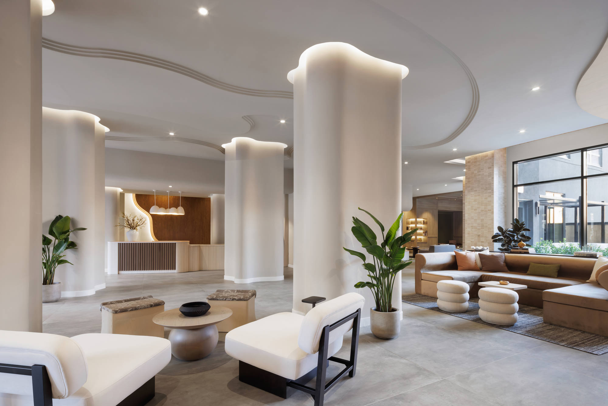 Expansive residential lobby lounge boasting fluid architectural ceilings, curved white accent pillars, modern white armchairs, a large sectional sofa, and floor-to-ceiling windows.