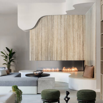 Close-up of a modern lounge area showcasing a curved stone bench wrapped around a linear flame fireplace, framed by a striking vertical-grain stone statement wall.