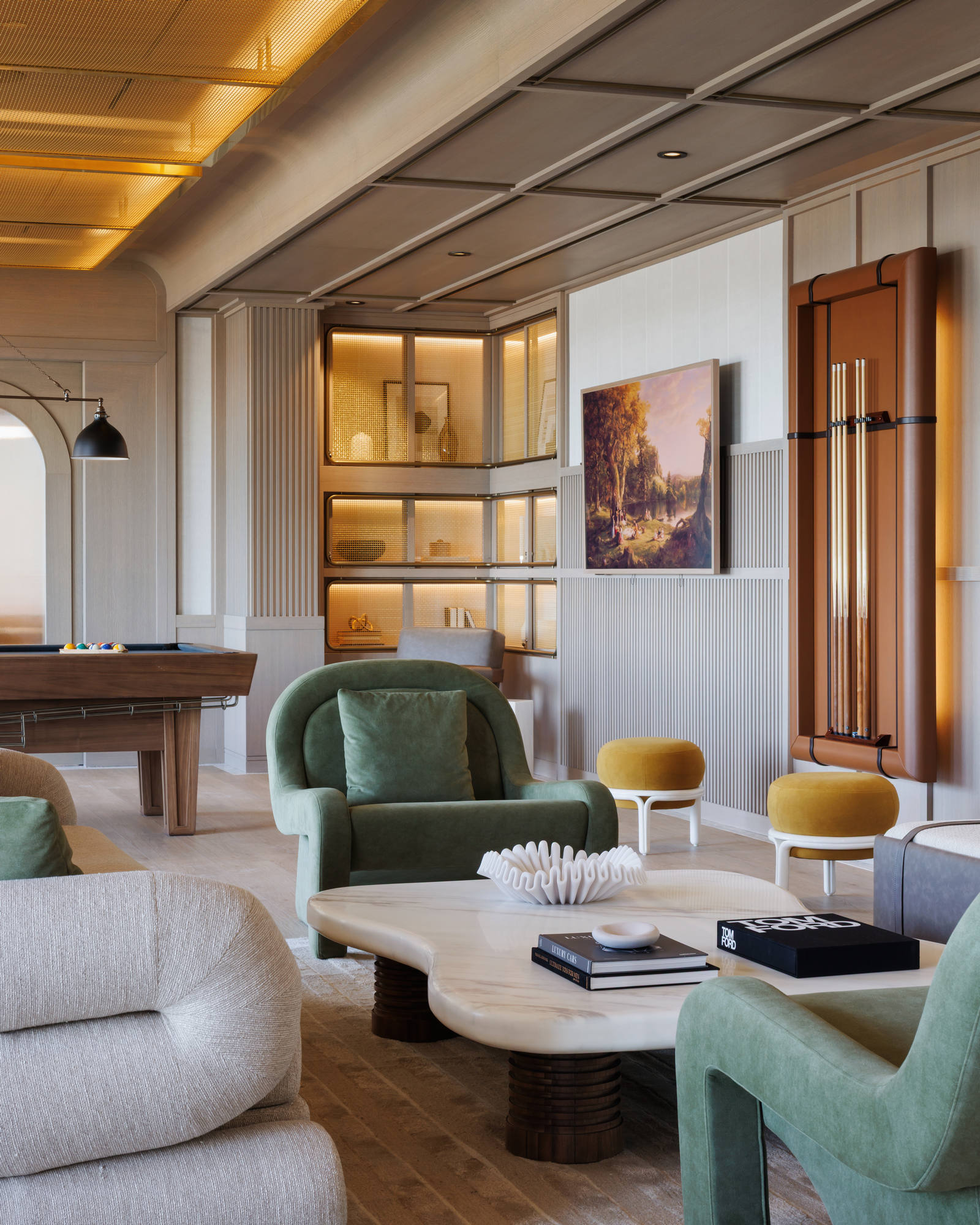 Mid-century modern style media and game lounge featuring a premium wood billiards table, custom recessed wall shelves with warm accent lighting, green velvet armchairs, and a wall-mounted cue rack.