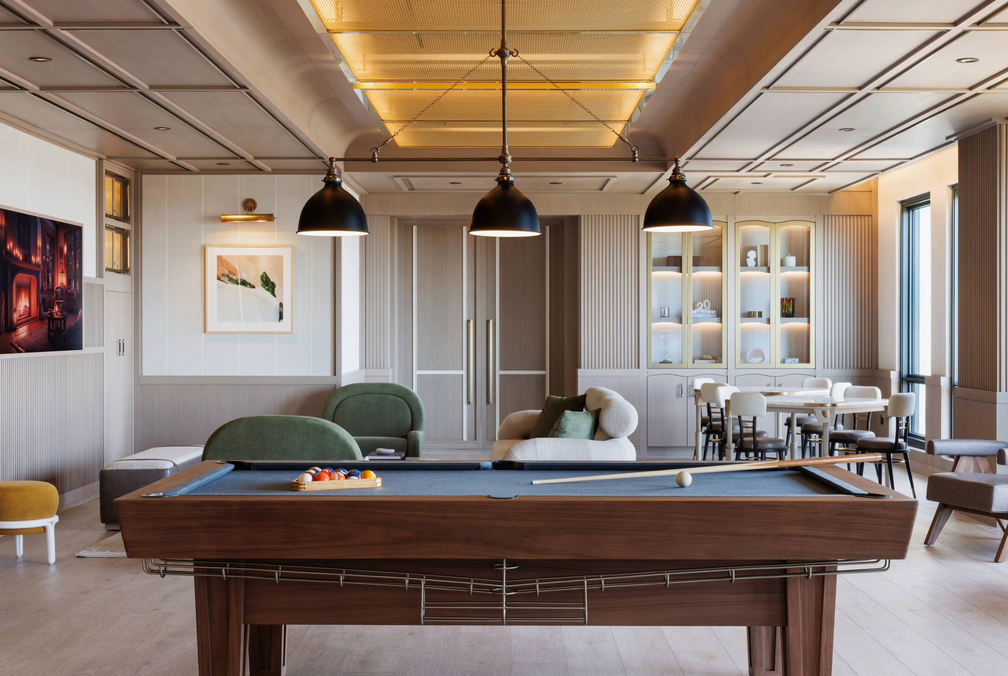 Straight-on view of a luxury billiards room highlighting a dark felt pool table, built-in lighted shelving units, a leather bench with small white side tables, and elegant wood paneling.