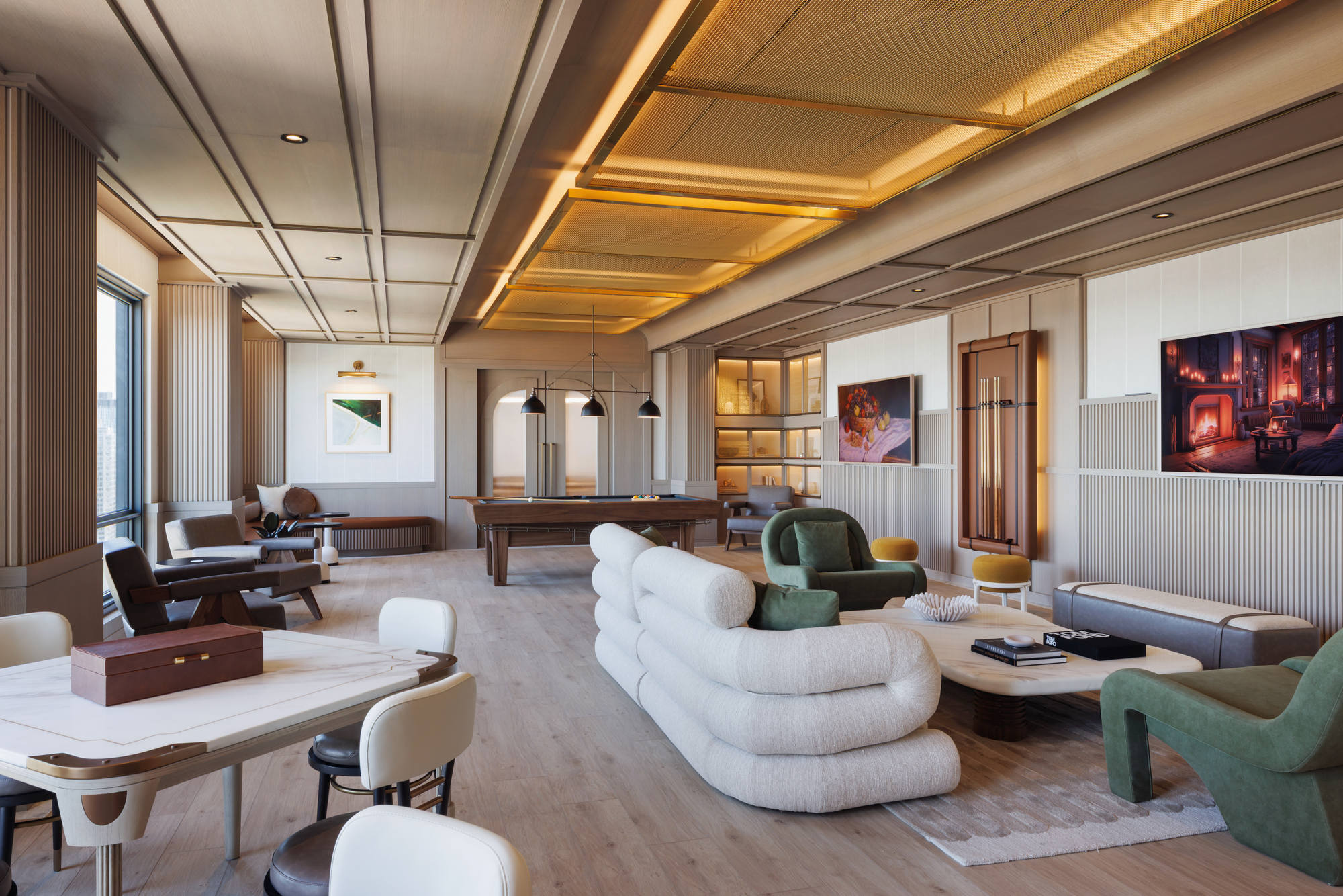 Open-concept community game and media lounge, showcasing a multi-textured ceiling with golden mesh paneling, plush curved sectional sofas, a billiards table, and card tables.