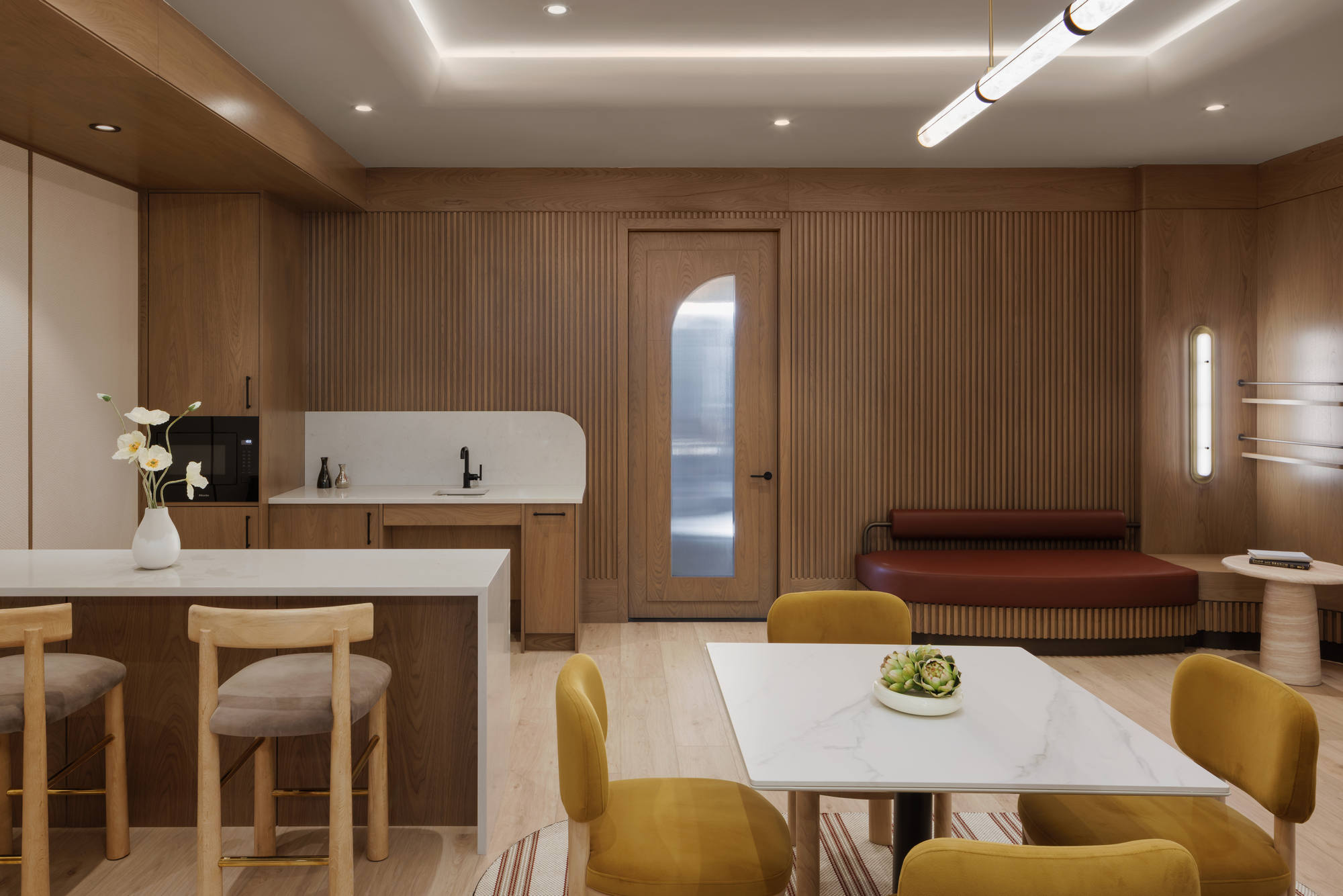 Premium resident co-working suite boasting custom wood-slat wall paneling, white quartz countertops, a kitchen island with barstools, and modern light fixtures.